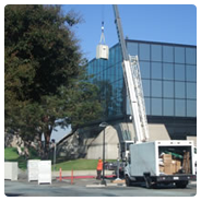 Straight truck and a crane in a parking lot with the crane hoisting up an emergency power supply to the roof of a building